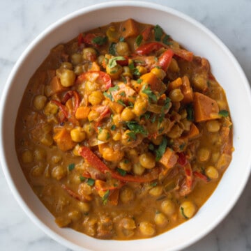 Chickpea and sweet potato curry with red bell pepper, and chopped cilantro in a white bowl.