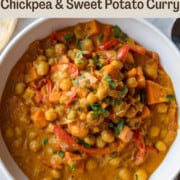 Chickpea and sweet potato curry with red bell pepper, and chopped cilantro in a white bowl with a silver spoon alongside.