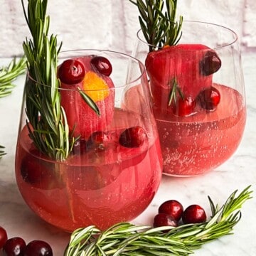 Cranberry mocktails in two glasses with mocktail ice cubes, sparkling water, fresh cranberries, and fresh rosemary.