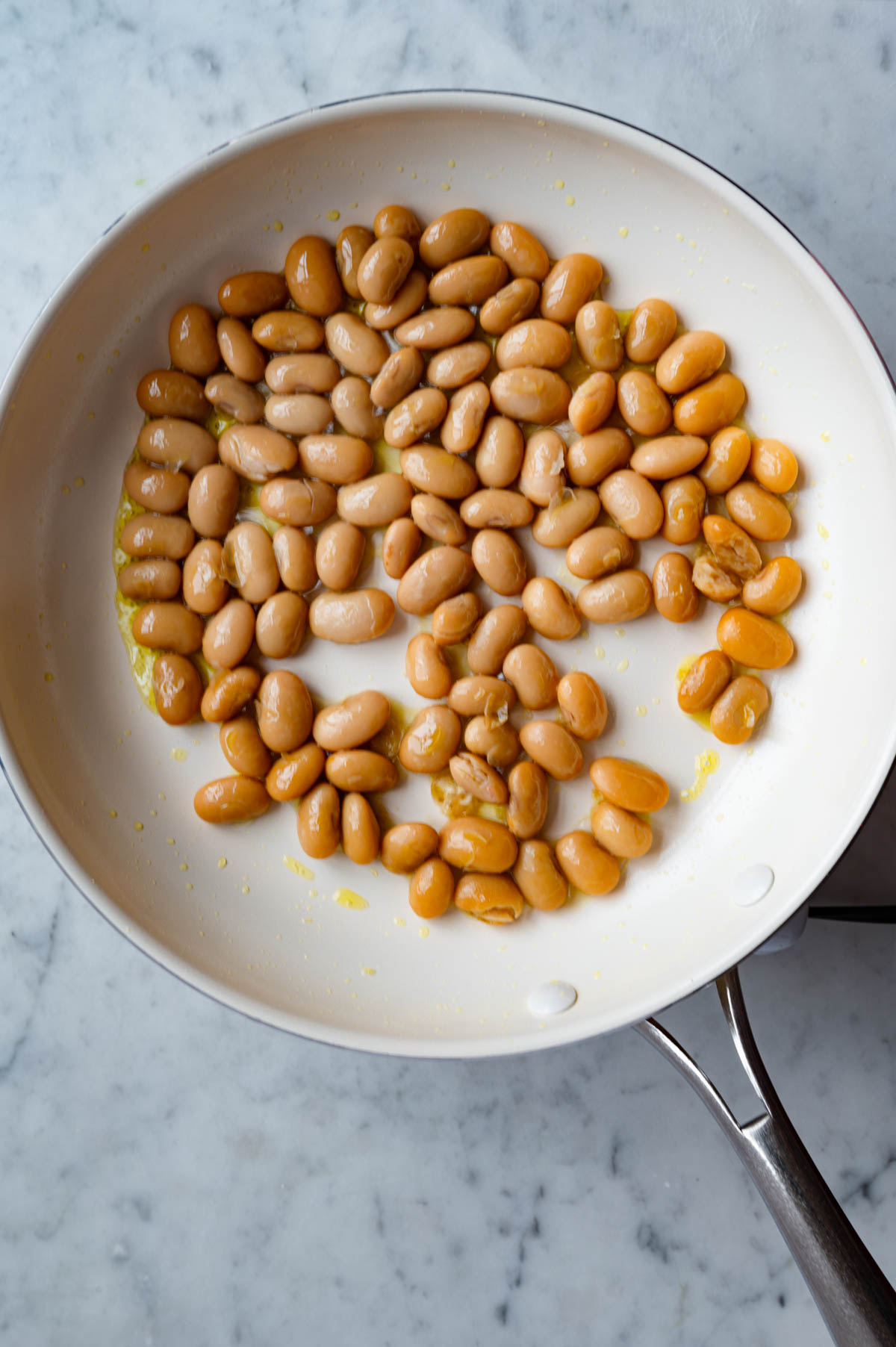 Pan fried golden butter beans in a white skillet.