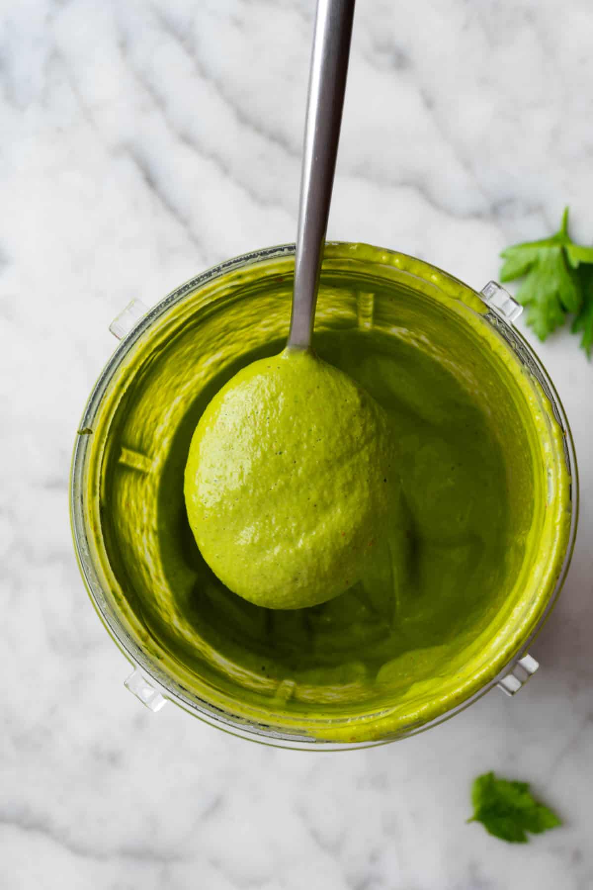 Healthy green goddess dressing in the canister of a blender with a silver spoon.