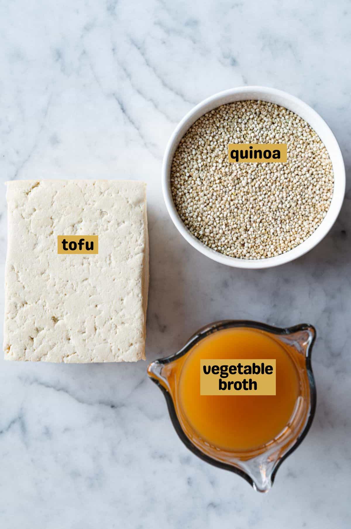Dry quinoa in a white bowl with vegetable broth, and a block of extra-firm tofu.