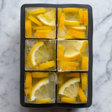 Six ice cubes with frozen lemon ginger tea and cut lemon wedges.