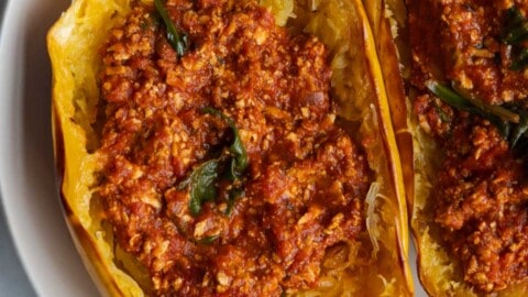 Tofu bolognese serves in spaghetti squash halves in a white bowl.