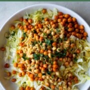 Cabbage salad topped with crispy chickpeas, parsley, and vegan Caesar dressing in a white bowl.