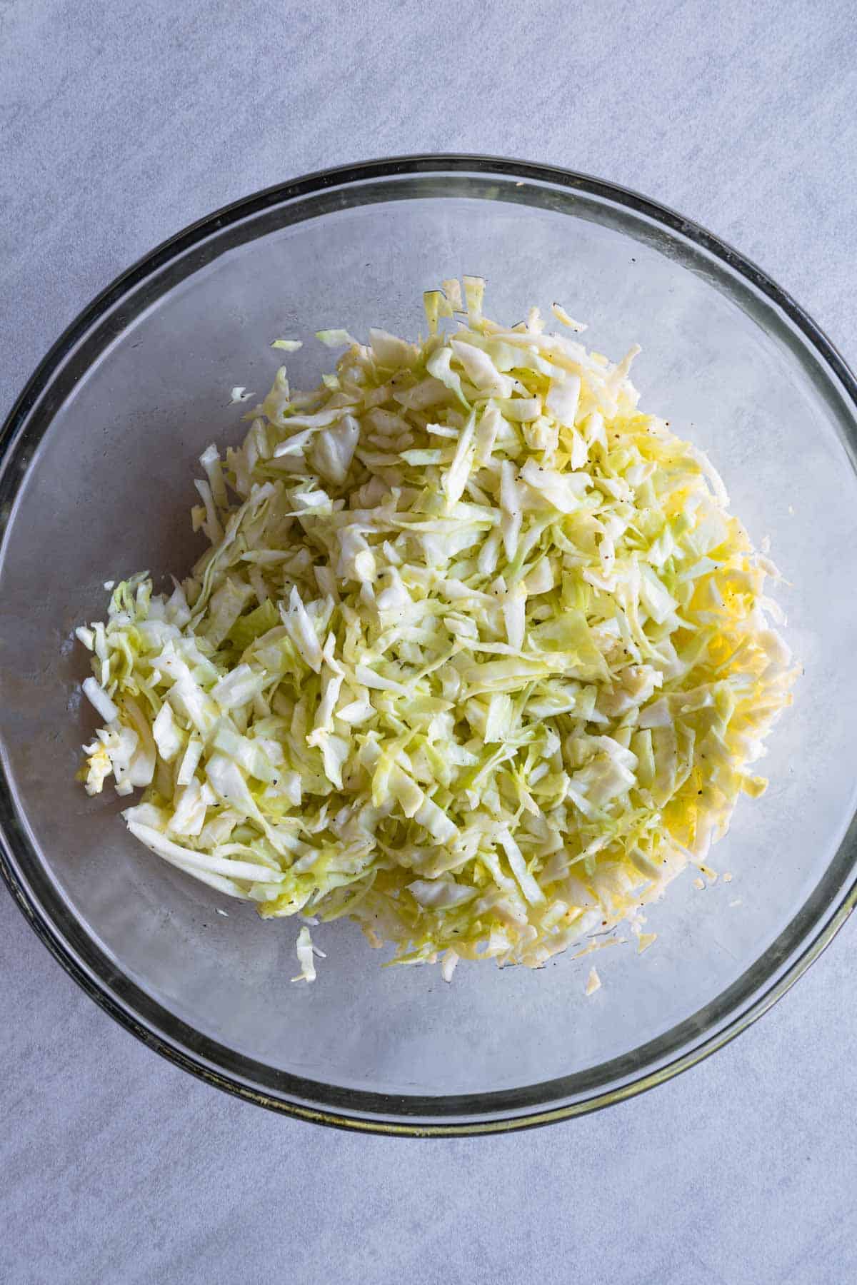 Shredded green cabbage tossed with olive oil and black pepper in a glass bowl.