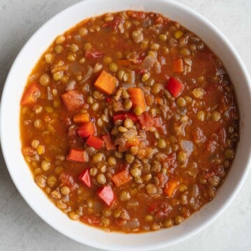 Lentil and carrot soup with red bell peppers, diced tomatoes, onion, and broth in a white bowl.