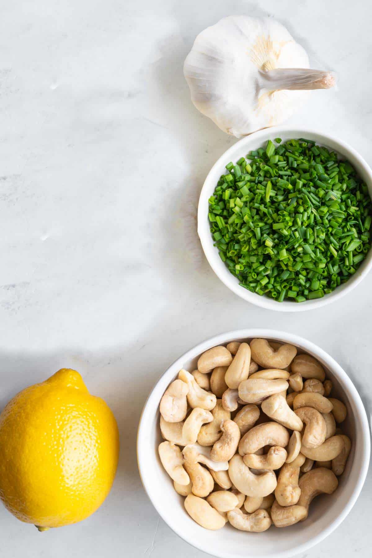 Garlic, lemon, cashews, and chopped chives in a white bowl.