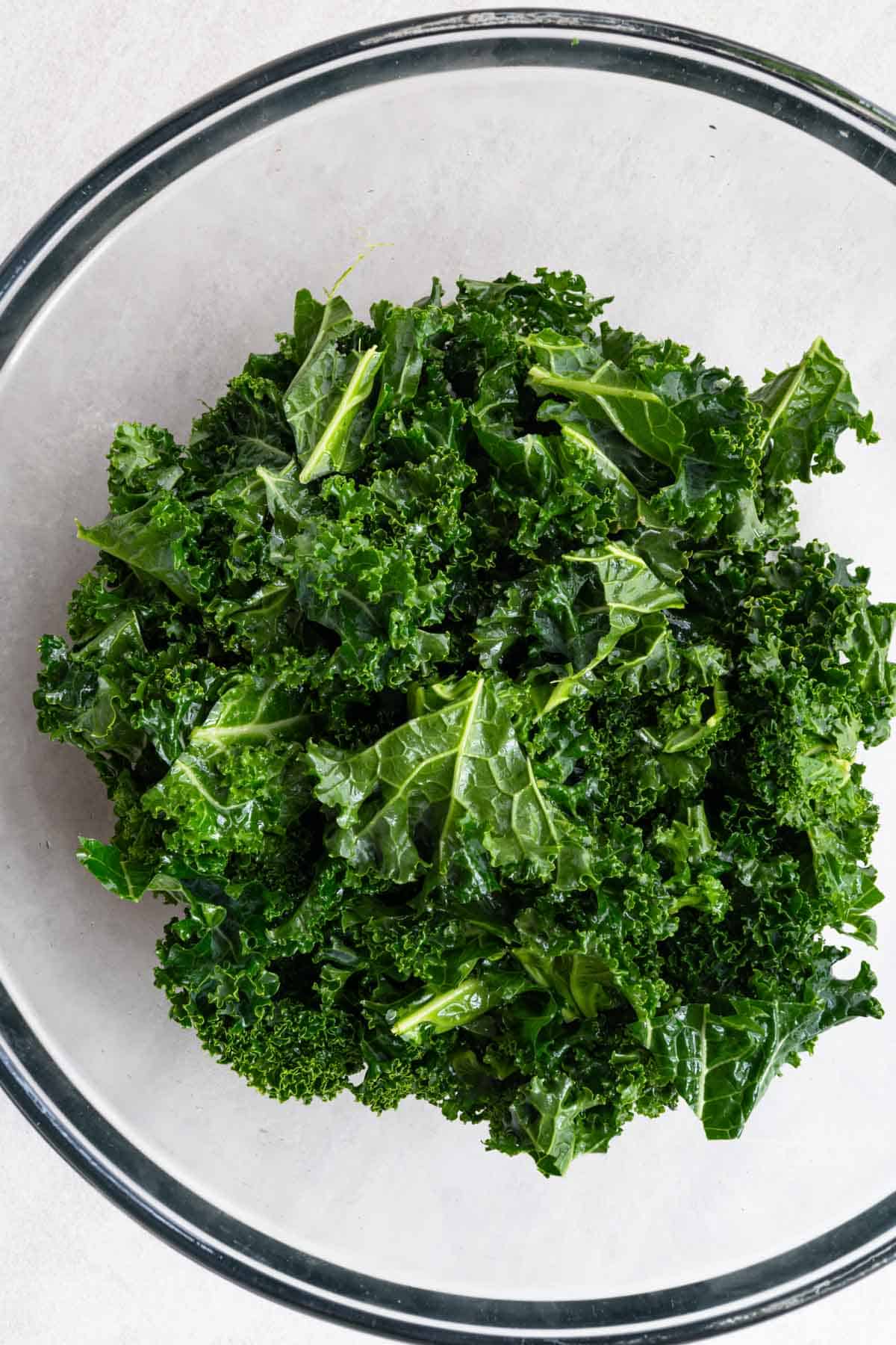 Chopped massaged kale leaves in a glass bowl.
