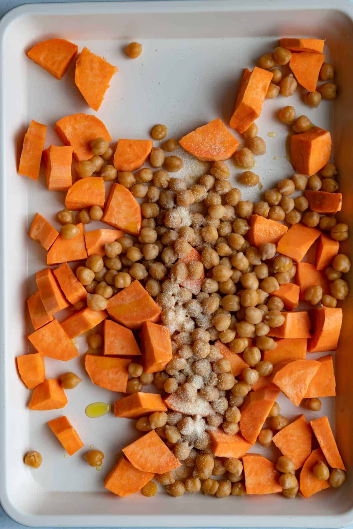 Cut sweet potato and chickpeas on a white rimmed baking sheet with garlic powder and olive oil.