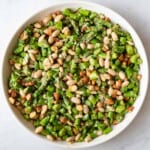 Chopped asparagus, white beans, almonds, miso dressing, and sesame seeds in a white bowl.