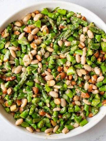 Chopped asparagus, white beans, almonds, miso dressing, and sesame seeds in a white bowl.