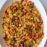 Couscous salad in a white oval platter with herbs, chopped bell pepper, green peas, chickpeas, carrots, curry dressing, and maple roasted cashews.