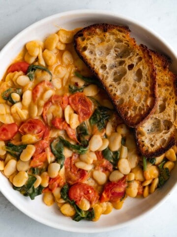 Creamy butter beans with grape tomatoes, spinach, and toasts in a white bowl.