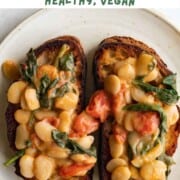 Creamy butter beans with grape tomatoes and spinach on two toasts on a white plate.