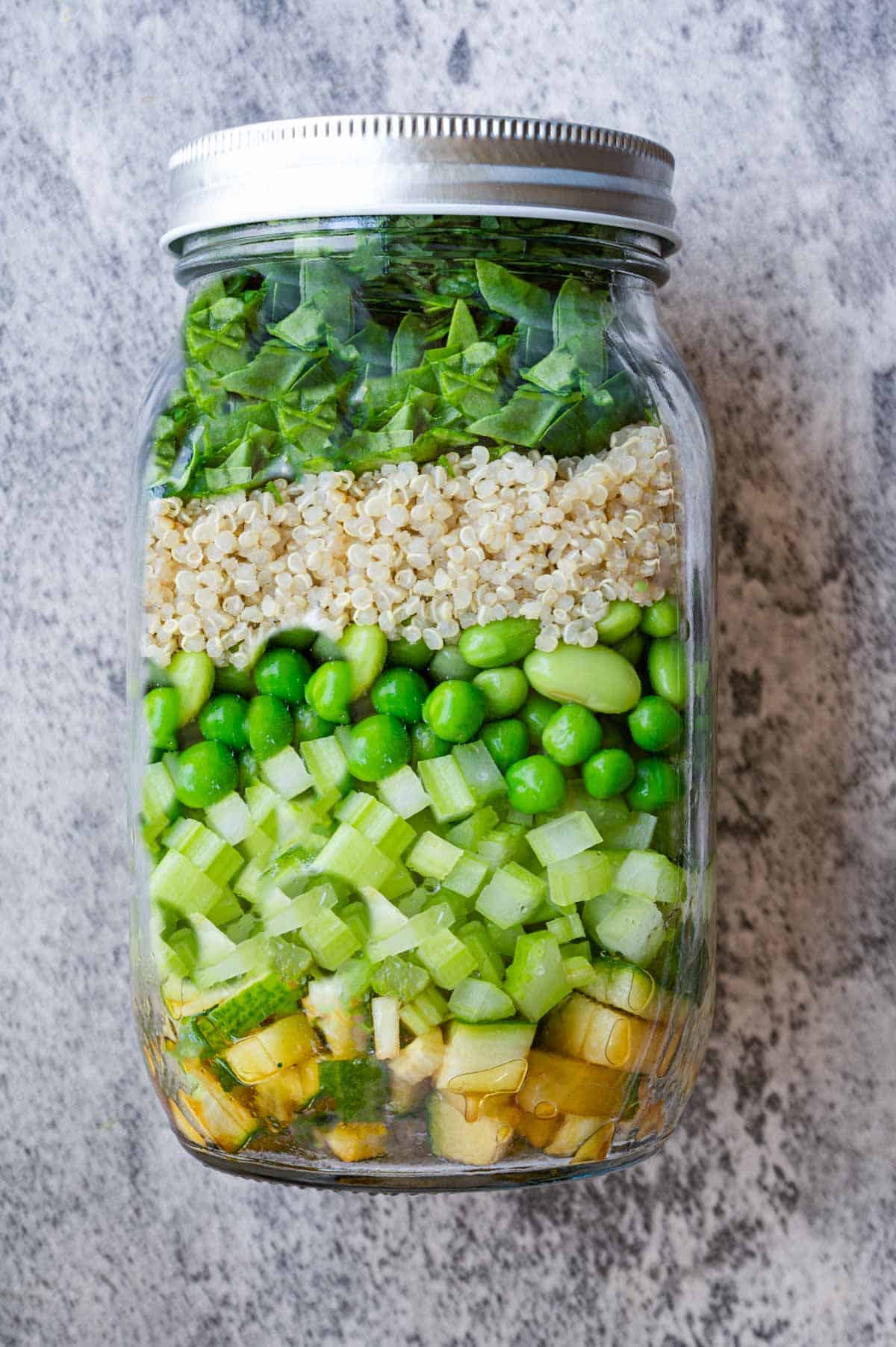 Layered salad mason jar with Asian dressing at the bottom. cucumber, celery, green peas, edamame, quinoa, chopped spinach and cilantro.