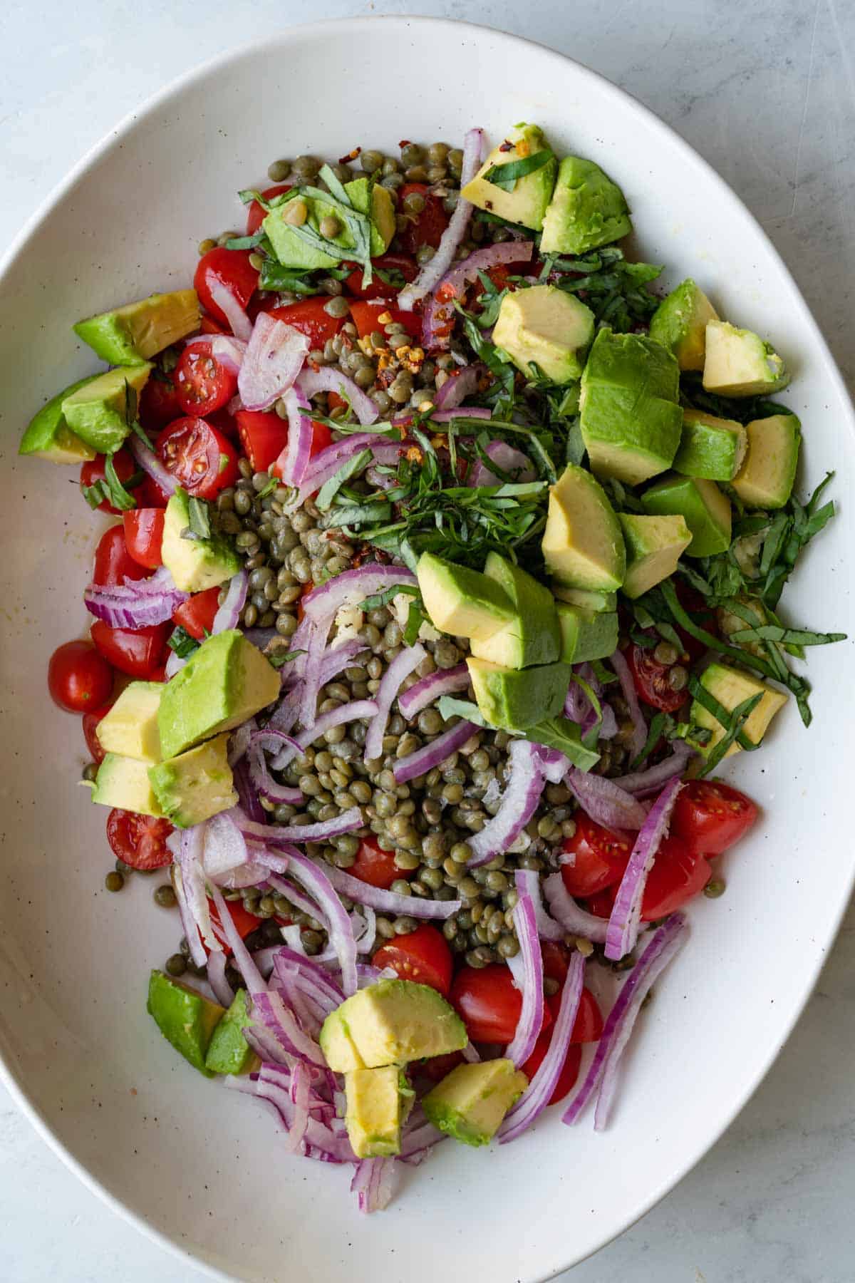 Tomatoes, avocado, legumes, red onion, and chopped basil in a white oval dish.