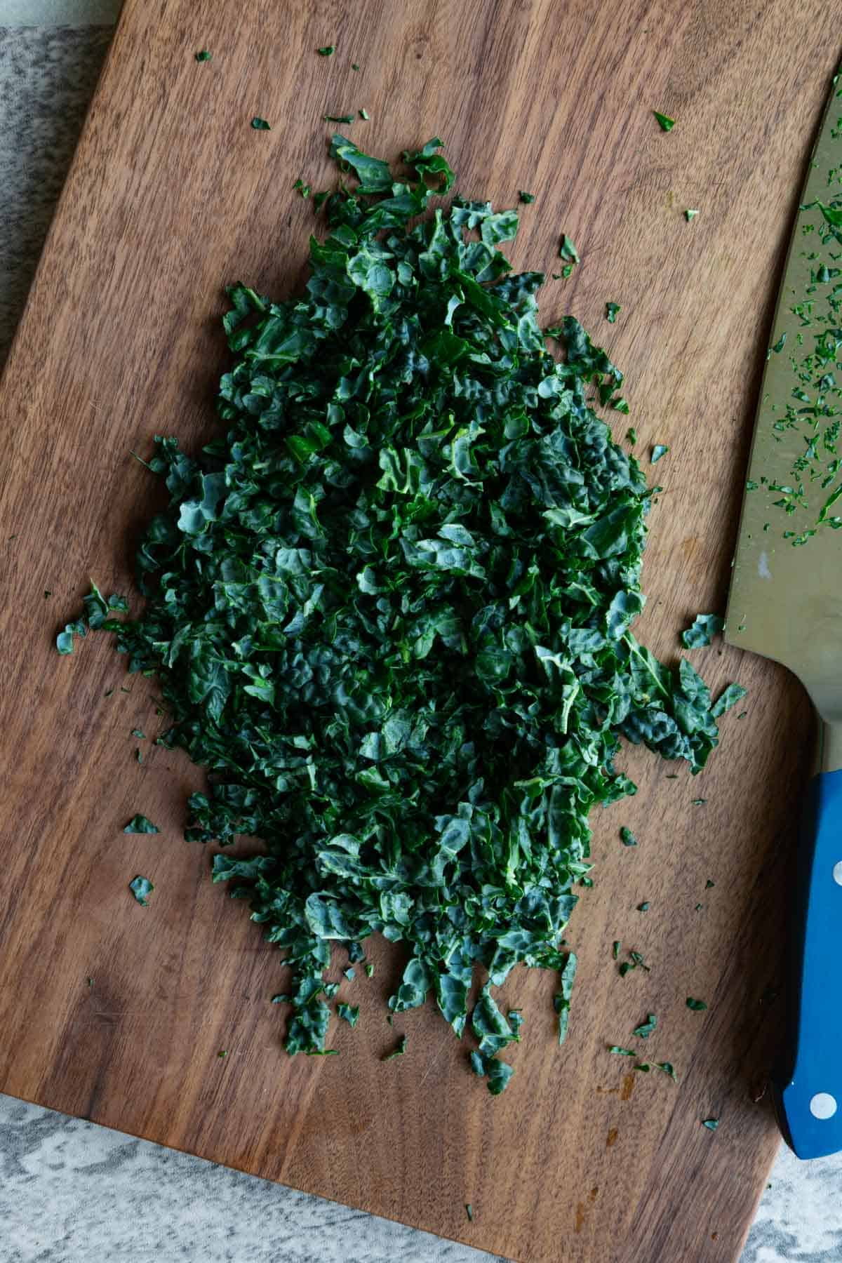 Chopped lacinato kale on a wooden cutting board with a blue handled chef's knife.