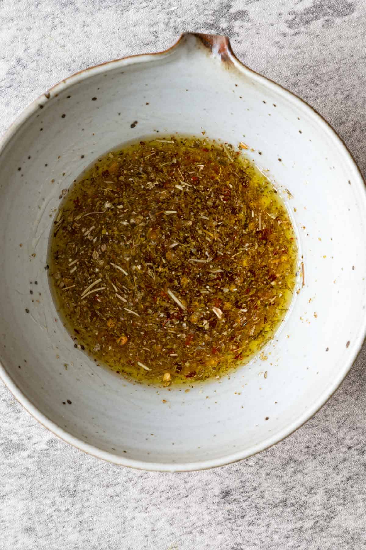 Dressing in a grey bowl made from olive oil, dried herbs, and vinegar.