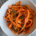Raw carrot salad in a white bowl with roasted pepitas, and chopped herbs.