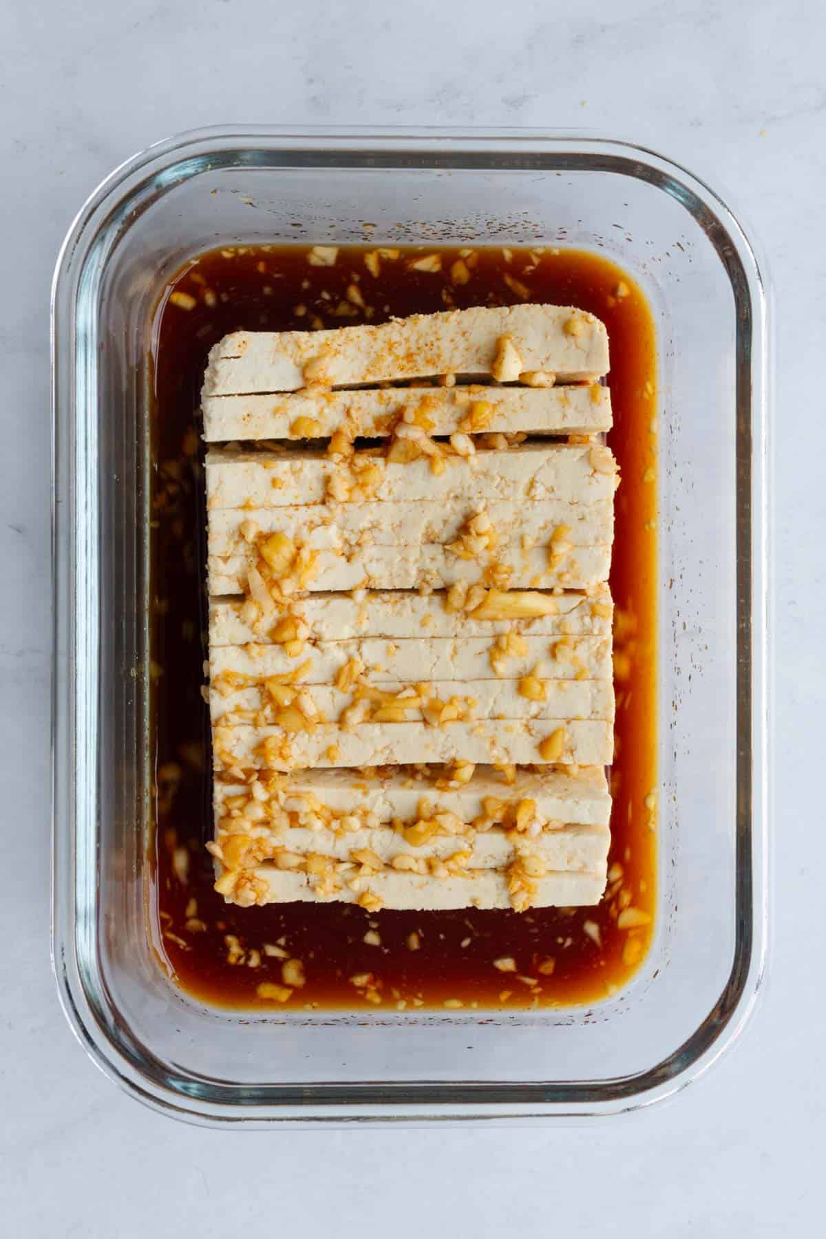 One sliced block tofu in a maple soy marinade in a glass container.