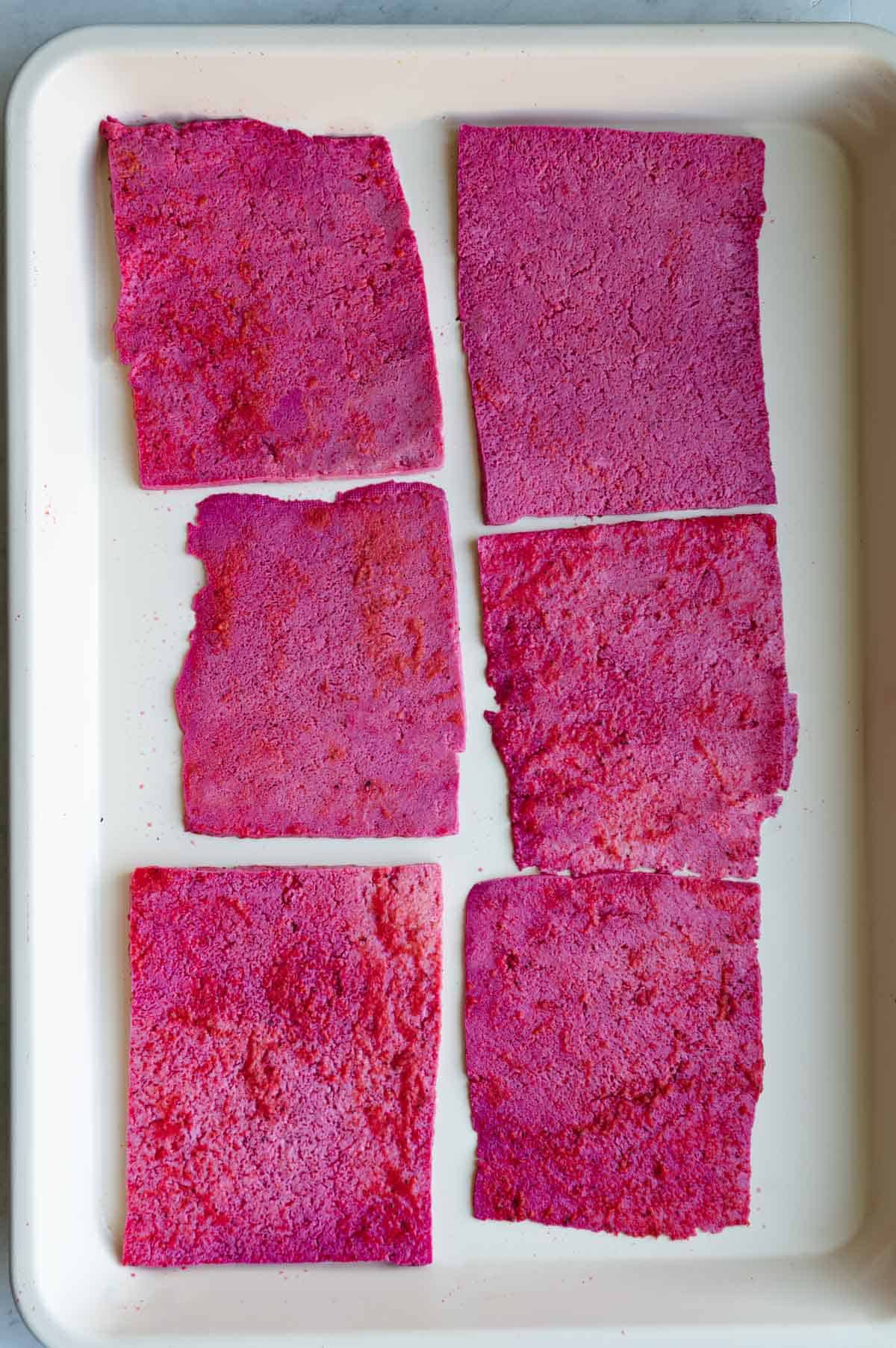 Finely sliced tofu rectangles soaked in beet brine on a white rimed baking sheet.