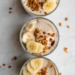 Banana chia pudding in three meal prep containers topped with banana slices and granola.
