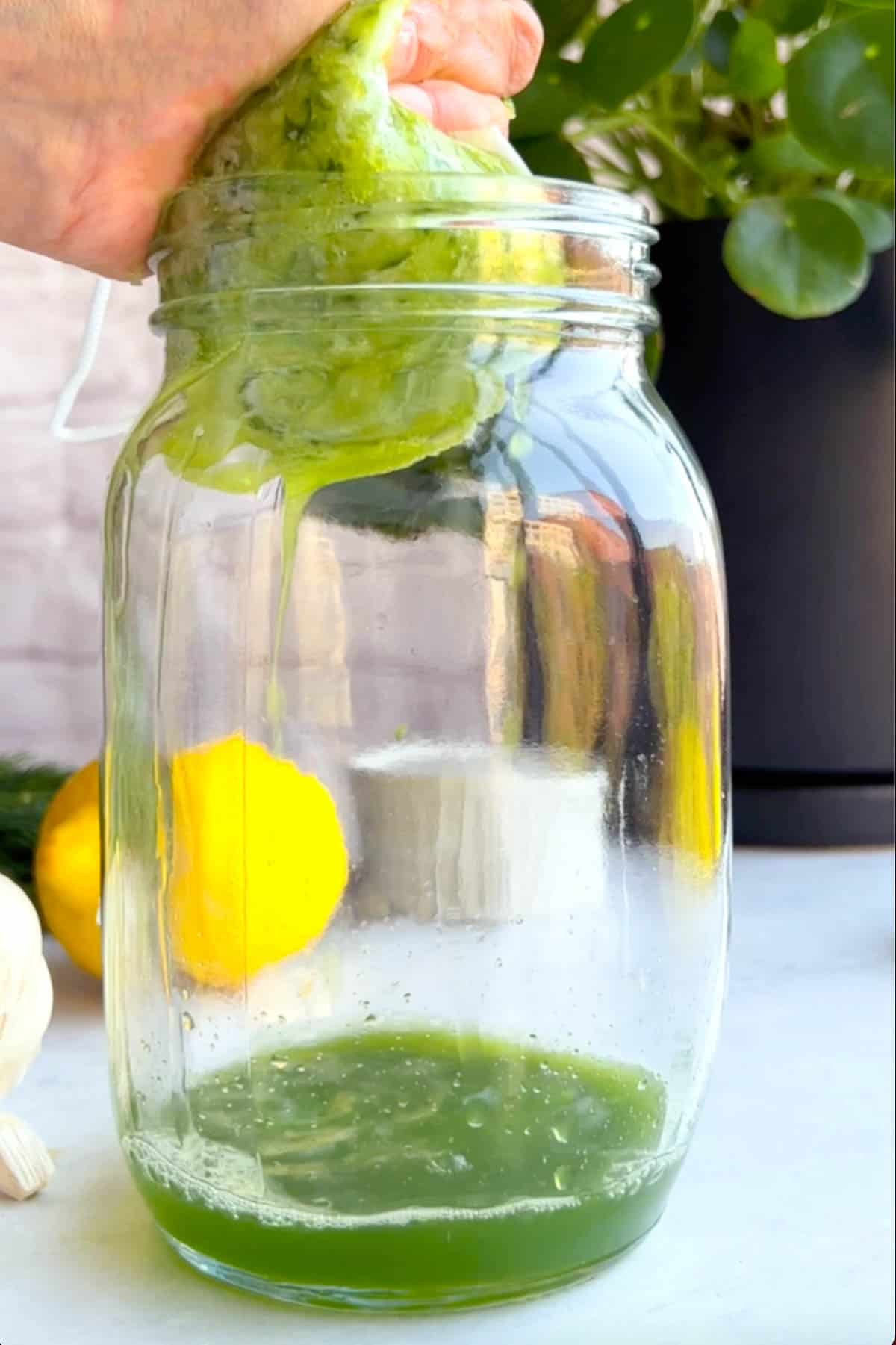 Grated cucumber in a nut bag being squeezed above a mason jar with green liquid draining into the jar.