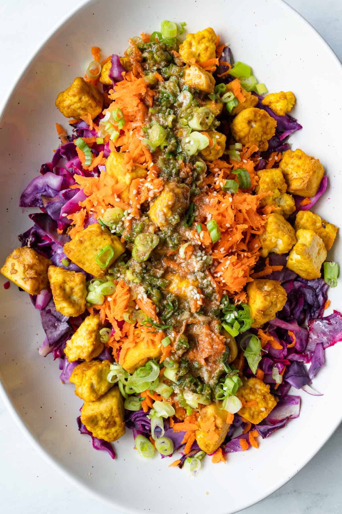 Tofu Salad with roasted tofu and red cabbage, grated carrots, chopped scallions, sesame seeds, and Asian dressing in a white oval bowl.