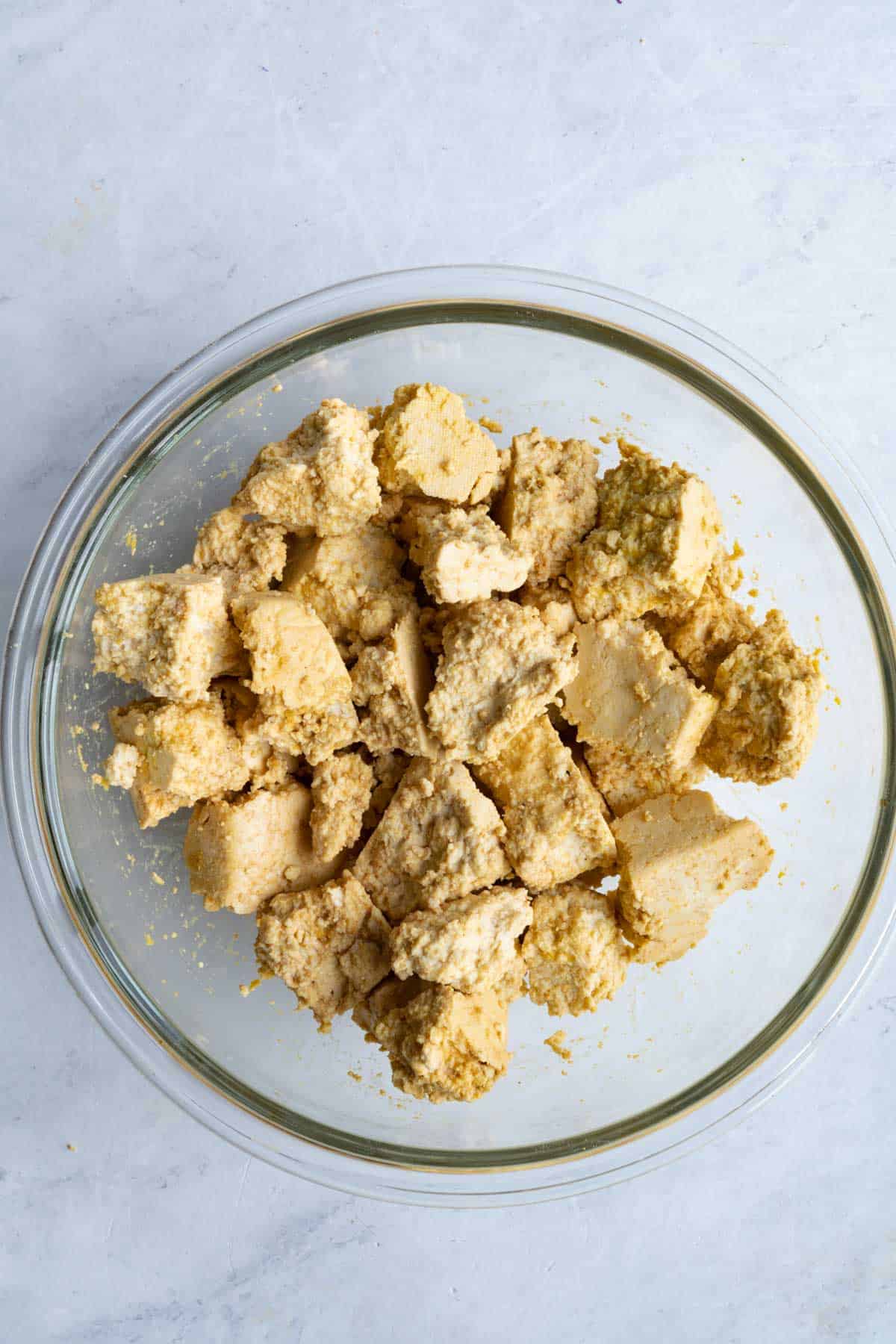 Chunks of tofu tossed in marinade in a glass bowl.