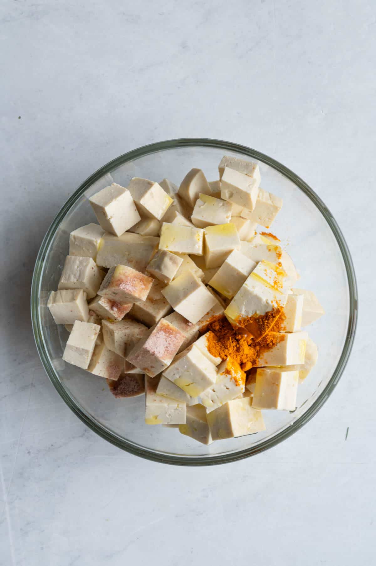 Cubed tofu in a glass bowl with turmeric, kala namak, and olive oil.