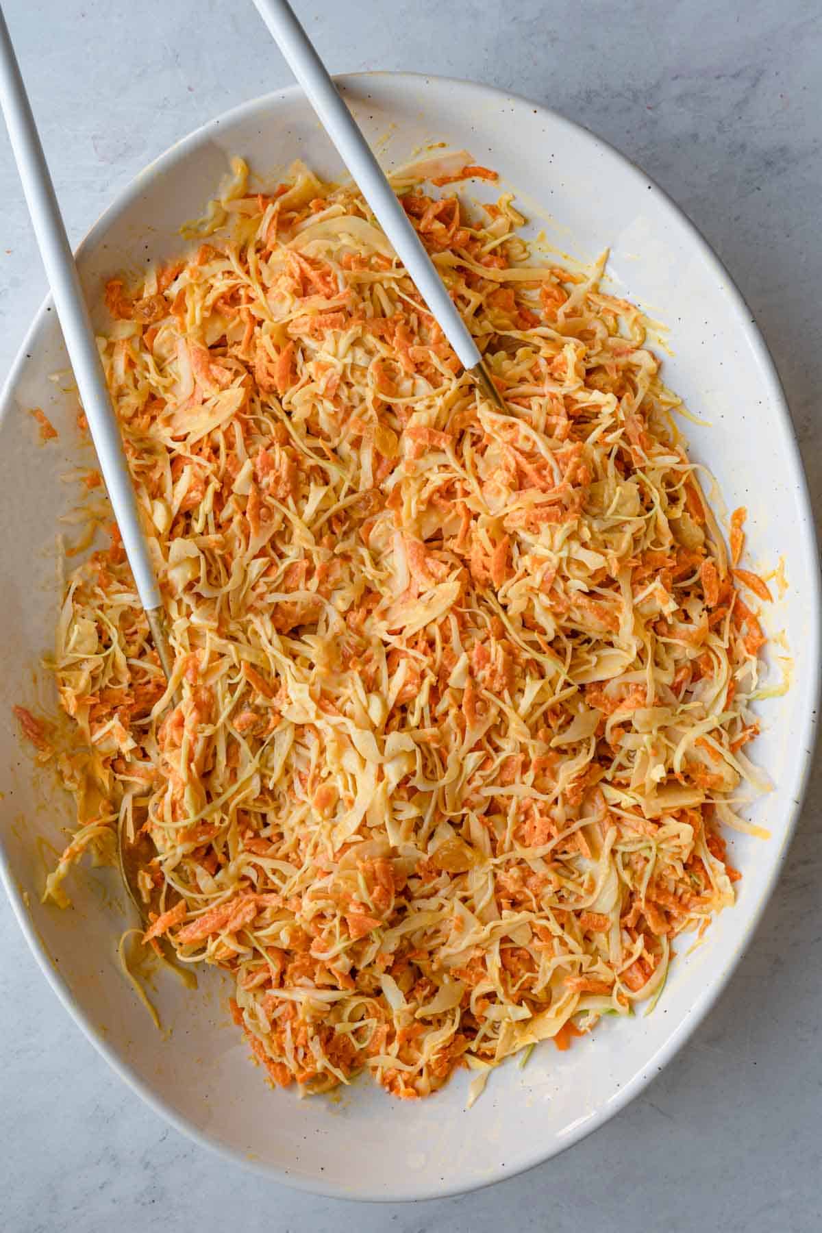 Vegan coleslaw in a large white oval bowl with salad servers.