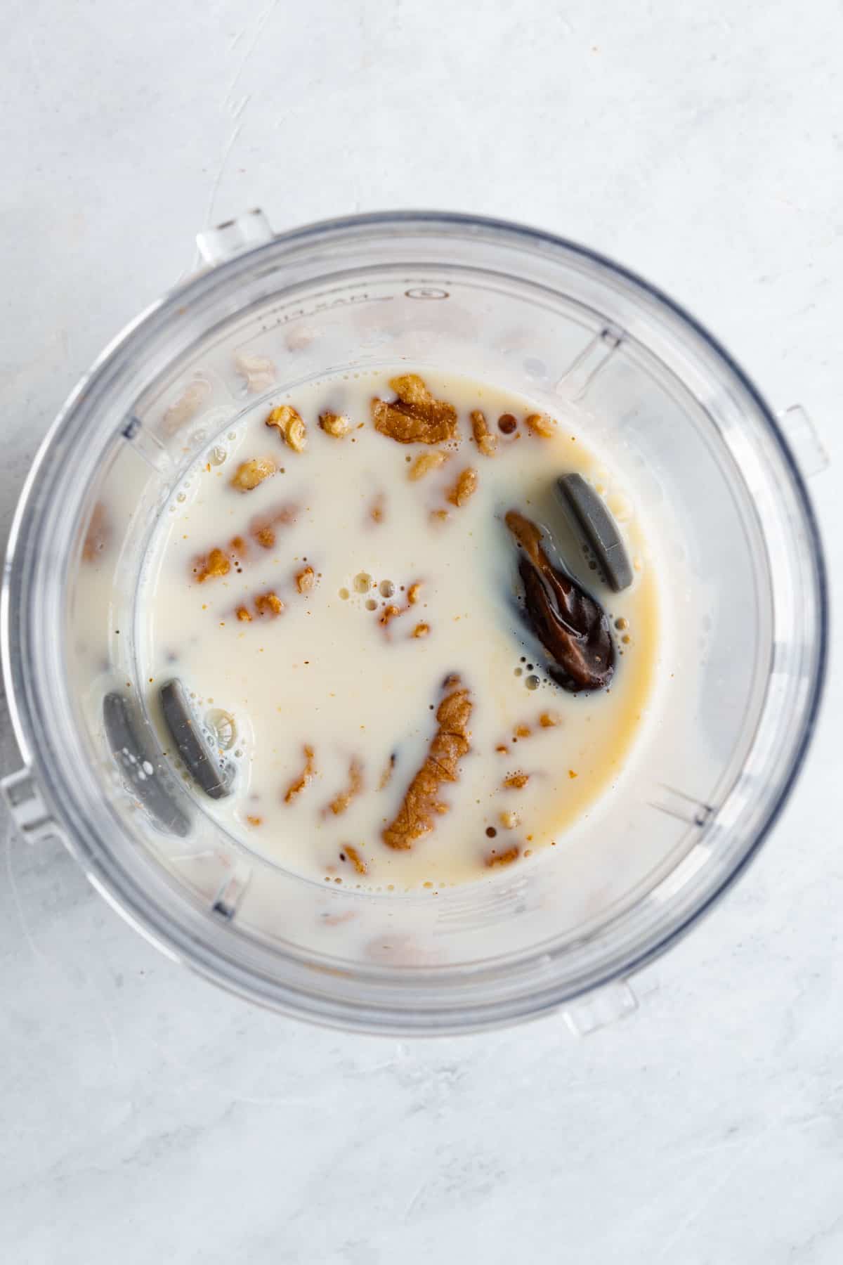 Nondairy milk, walnuts, and dates inside the canister of a blender.