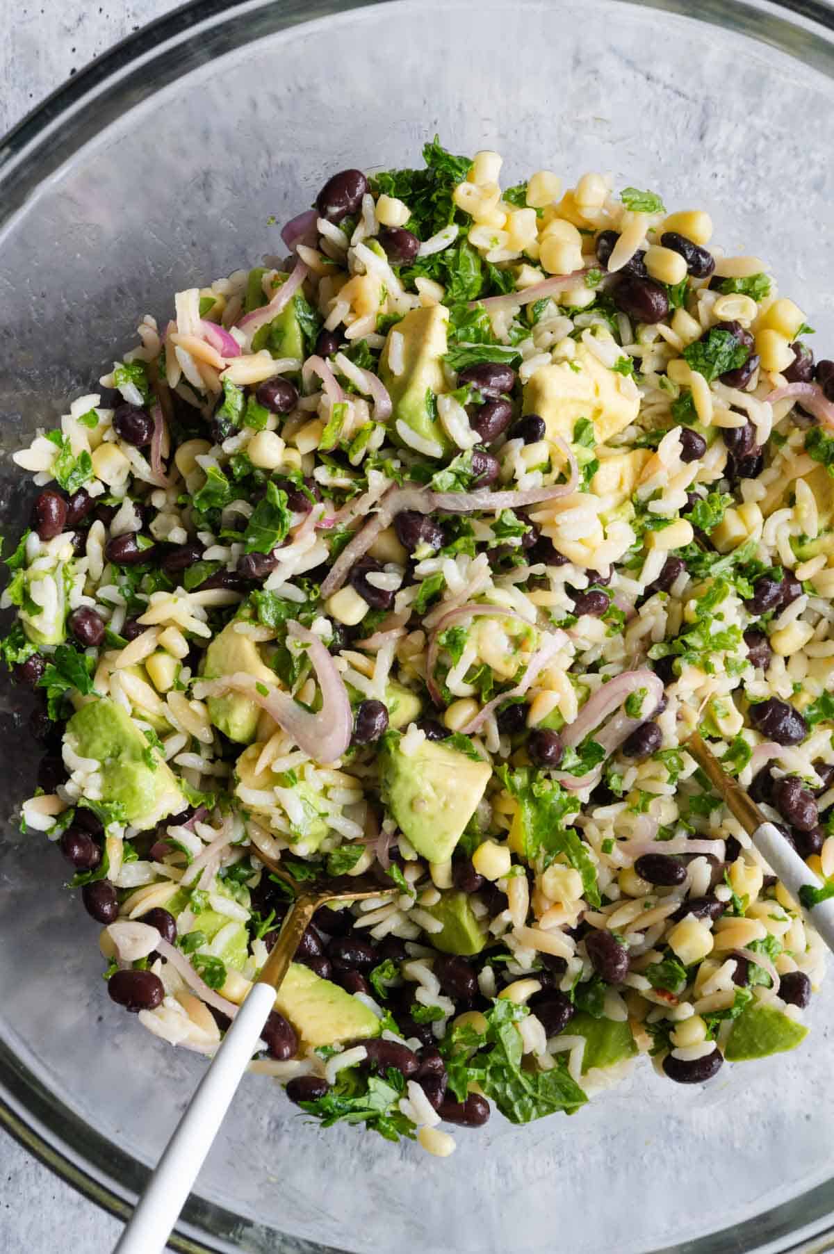 Black beans, avocado, corn, shallots, cilantro, kale, and orzo rice in a glass bowl.