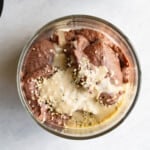 Edible cookie dough (chocolate) in a glass container, topped with tahini and hemp seeds.