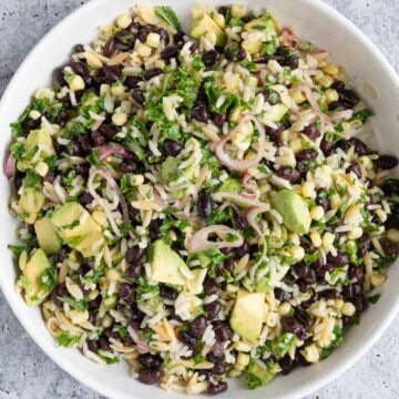Black beans, avocado, corn, shallots, cilantro, kale, and orzo rice in a white bowl.