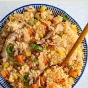 Rice cooker one-pot tofu rice bowl with shiitake mushrooms, green onion, corn, and carrots in a blue and white bowl with a golden spoon.