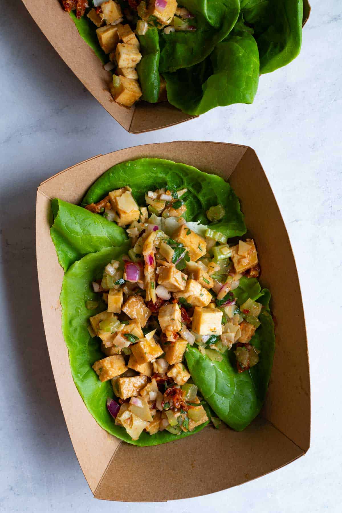 Marinated tofu salad with cubed baked tofu, chopped red onion, parsley, and celery served in lettuce wraps in paper baskets.