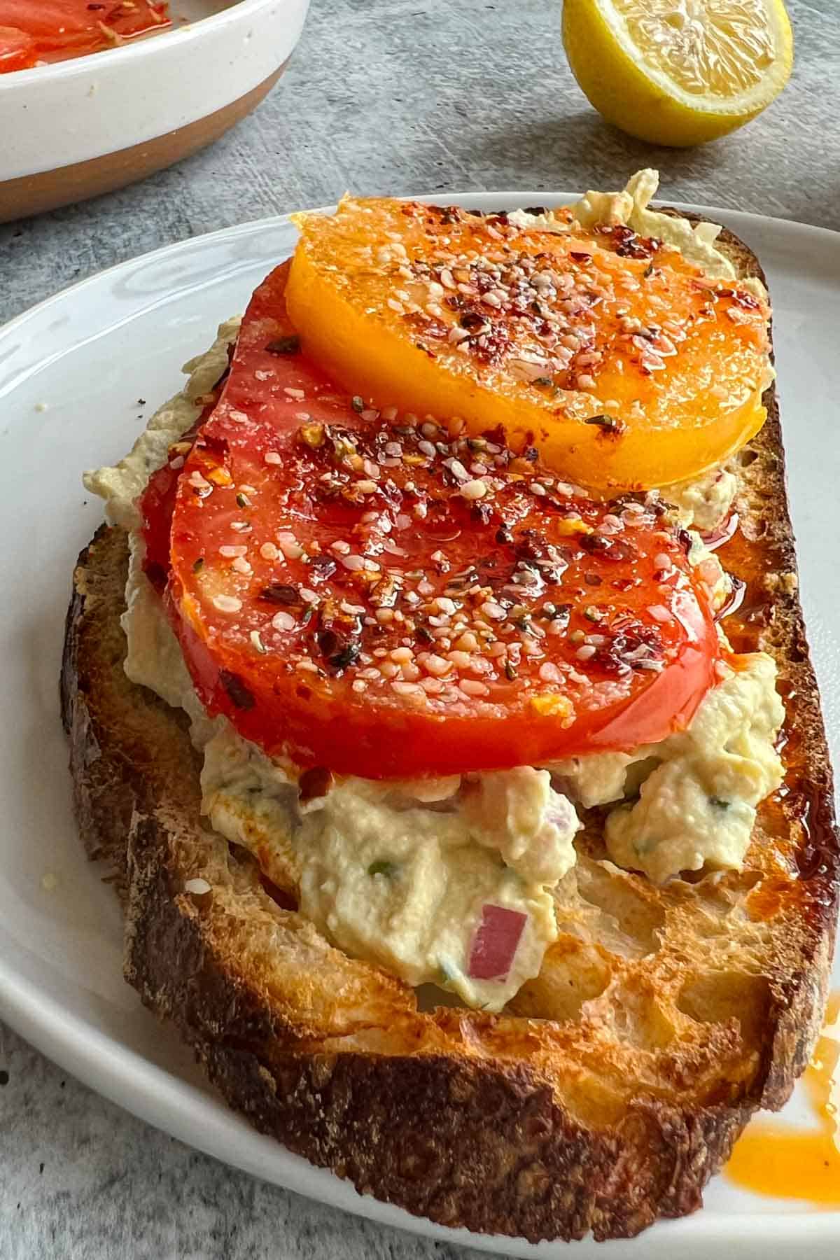 Vegan cream cheese with chives on sourdough toast with sliced tomatoes and chili crisp.
