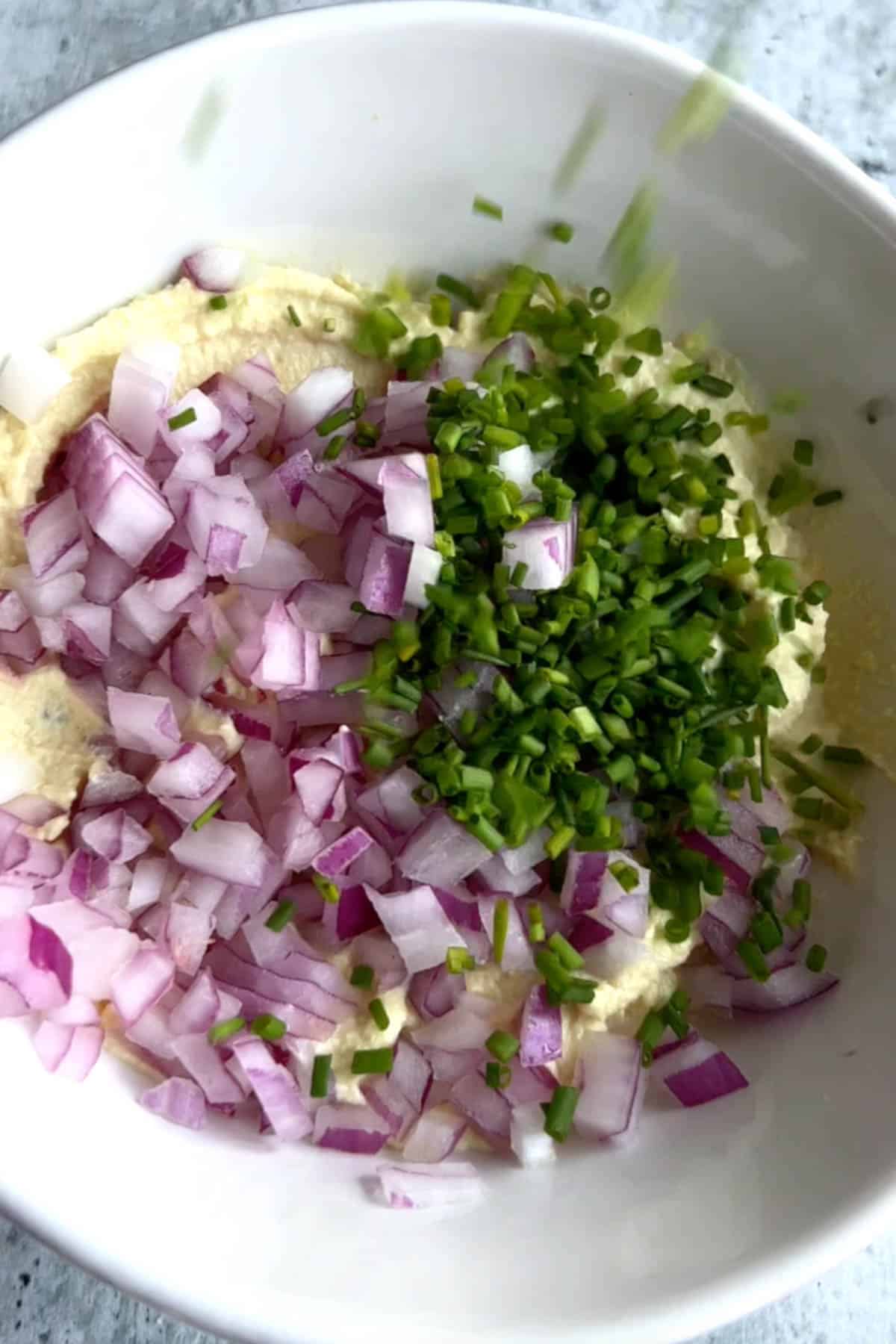 Vegan cream cheese, red onion, and chives in a white bowl.