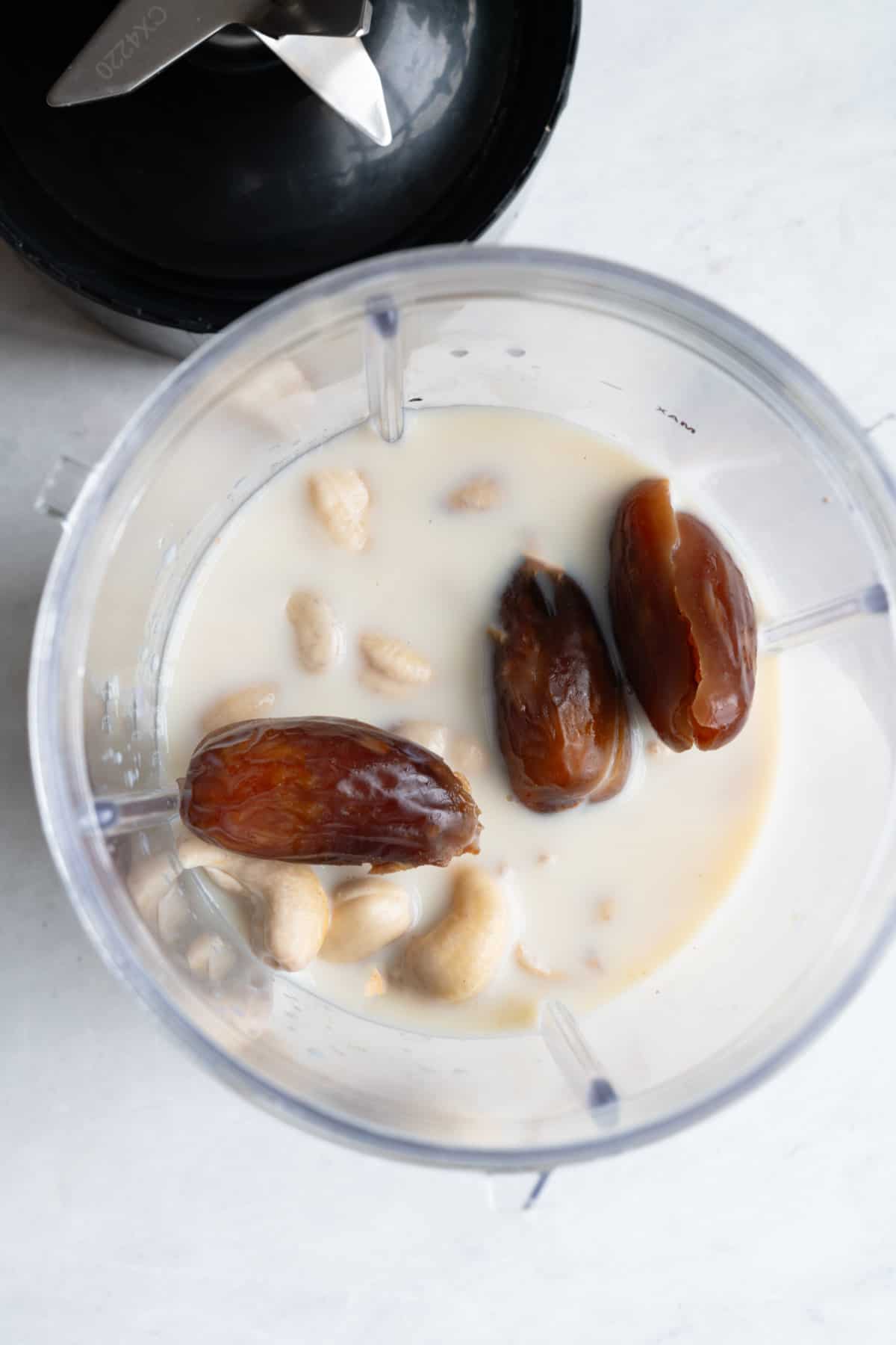 Dates, cashews, soy milk, and pecans in the canister of a blender.