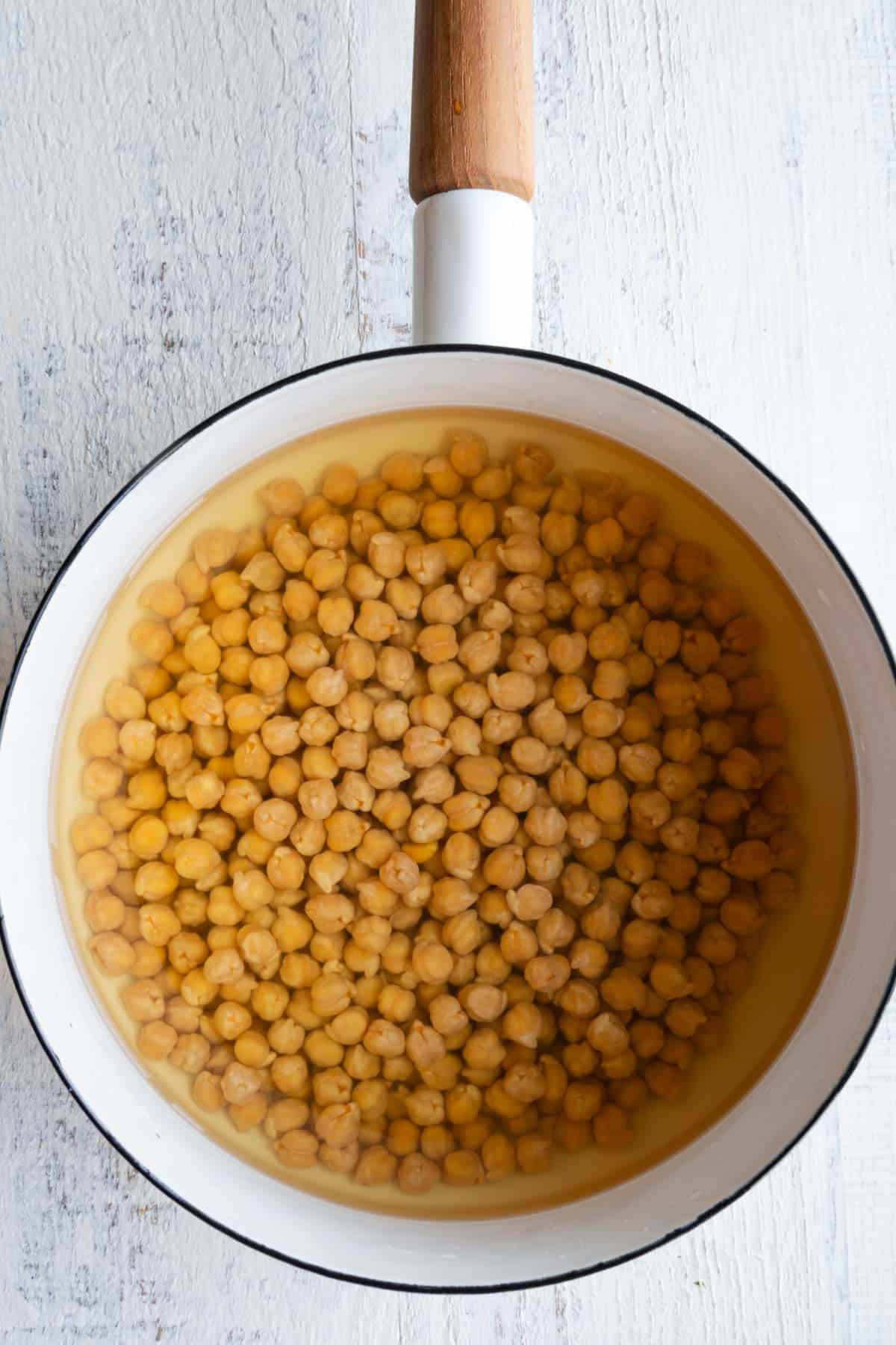Chickpeas soaking in water in a white saucepan.
