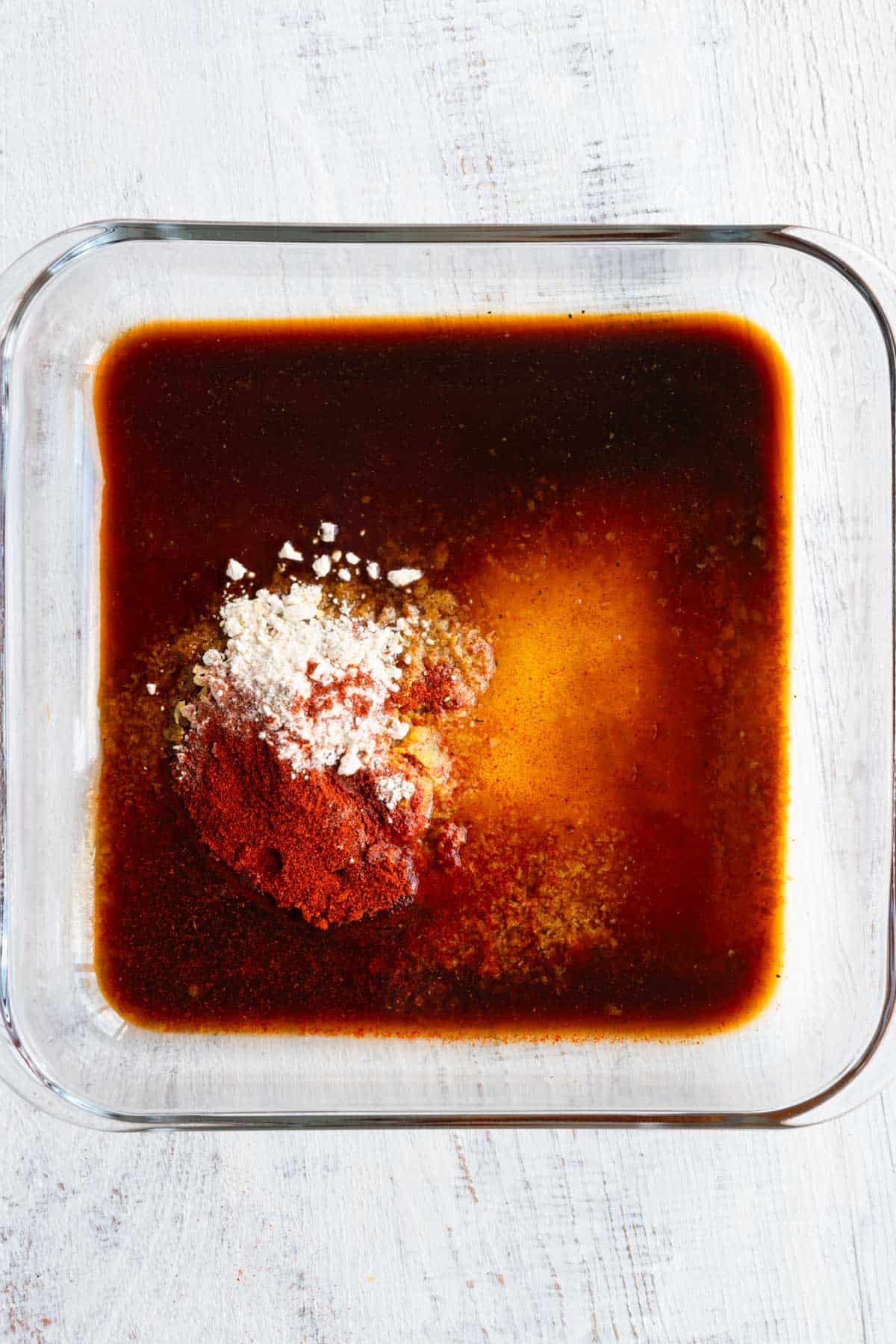 Red marinade in a square glass pyrex with red and white seasonings.
