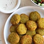 Golden brown vegan air fryer falafel in a white dish next to a cucumber tomato salad and white sauce.