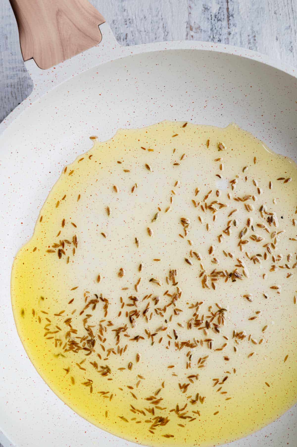Cumin seeds cooking in oil in a white skillet.