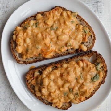 Creamy white beans skillet meal on two pieces of toast on a white plate.