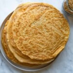 Red lentil flax seed wraps on a white plate next to a jar of flax seeds and a jar of red lentils.