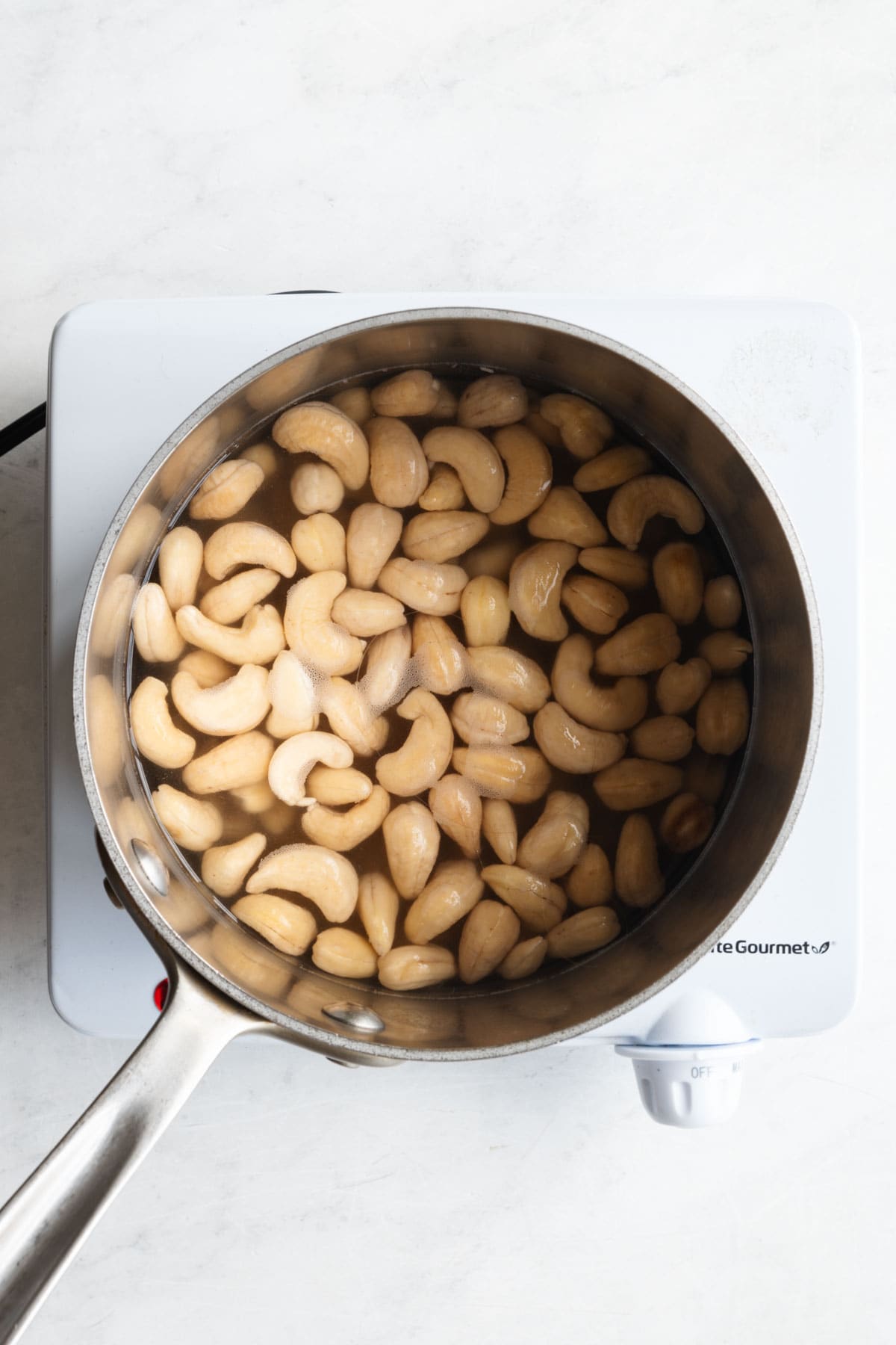 Cashews soaking in boiled water in a stainless stele saucepan.