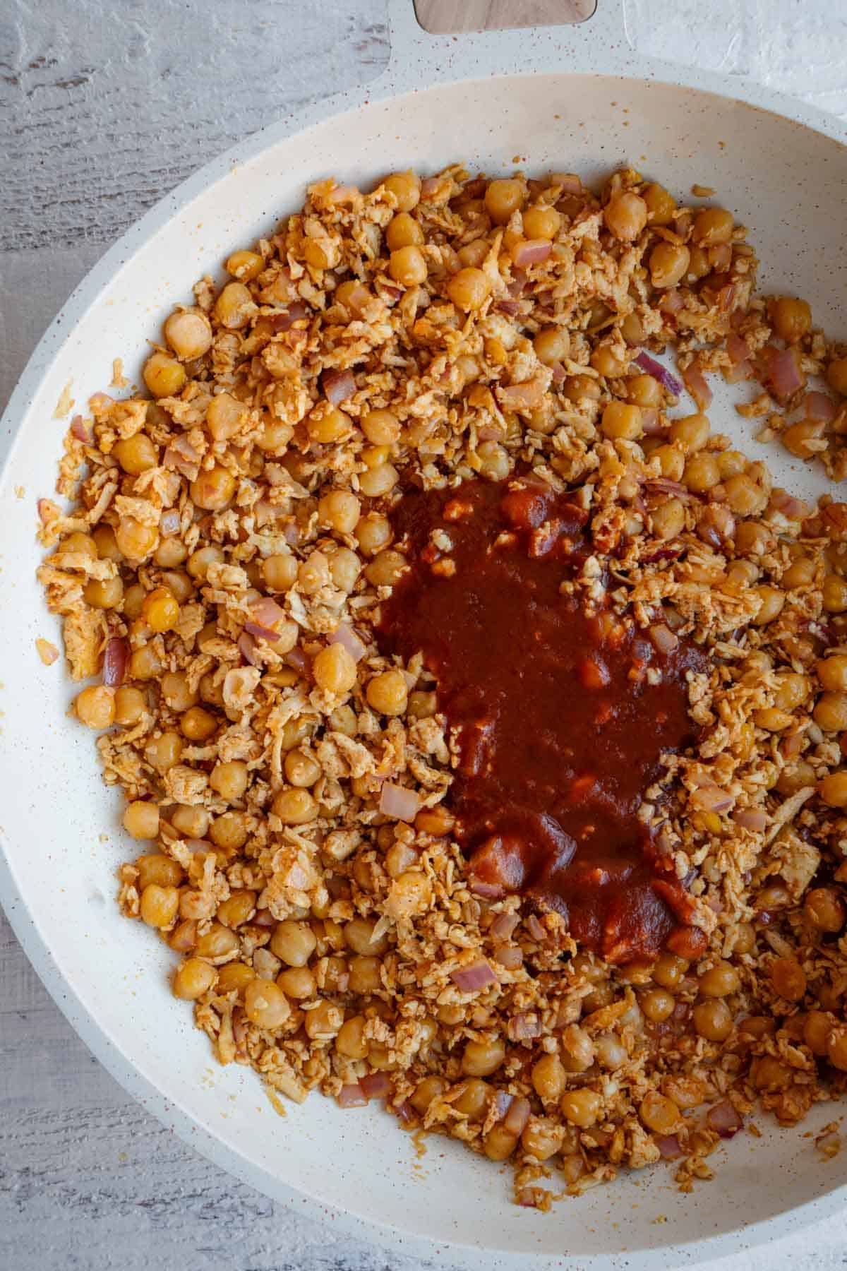 Tofu, chickpeas, and hot sauce cooking in a white skillet.