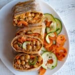 Two high-protein veggie wraps cut open on a white plate with a carrot and zucchini salad.
